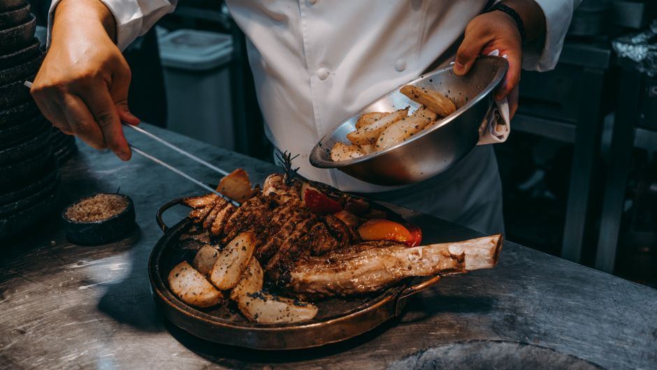 Chef cooking gourmet meat dish with roasted potatoes in a professional kitchen.