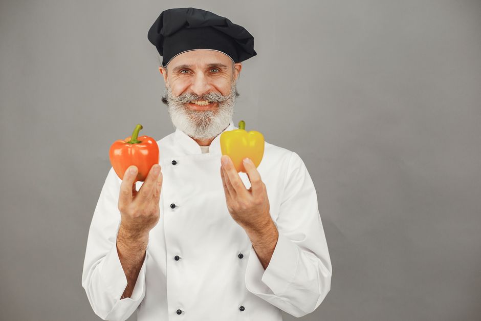 Portrait of a smiling chef in uniform holding red and yellow bell peppers. Ideal for culinary and food-related themes.
